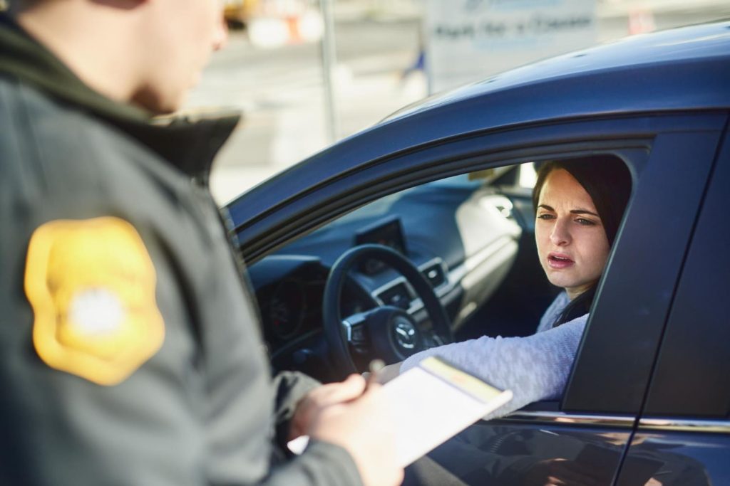 mulher dentro do carro reclama ao receber multa do agente de trânsito